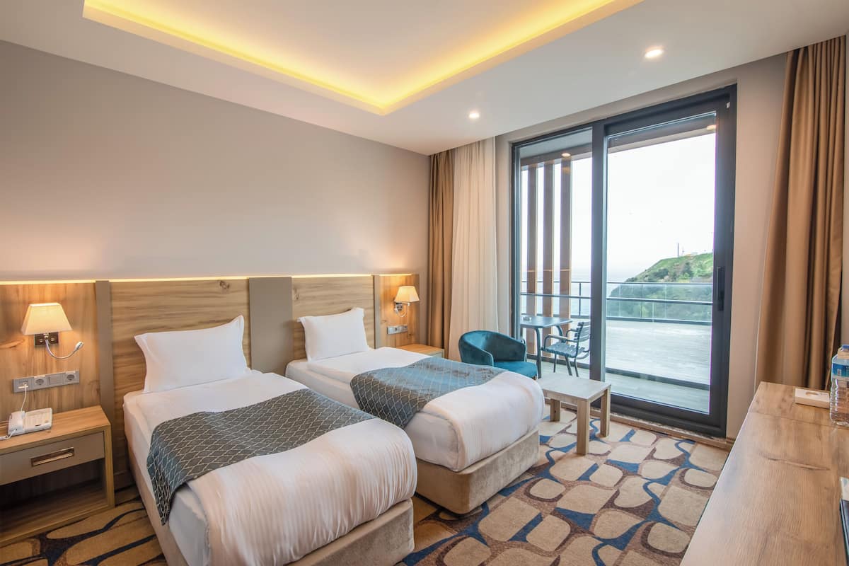 Ein Hotelzimmer mit zwei Betten, einem Schreibtisch, einem Stuhl und einem großen Fenster mit Blick auf ein Gewässer.