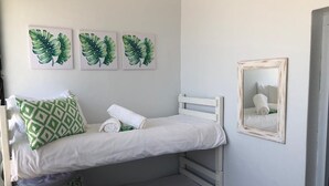 Ein Schlafraum mit Etagenbetten, weißer Bettwäsche, Kissen mit grünem Muster und drei Wandbildern mit Blattmotiven.