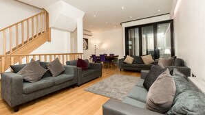 A modern living room with two grey sofas, a wooden staircase, and a dining area in the background. - Gorgeous house in the heart of Chelsea (London)