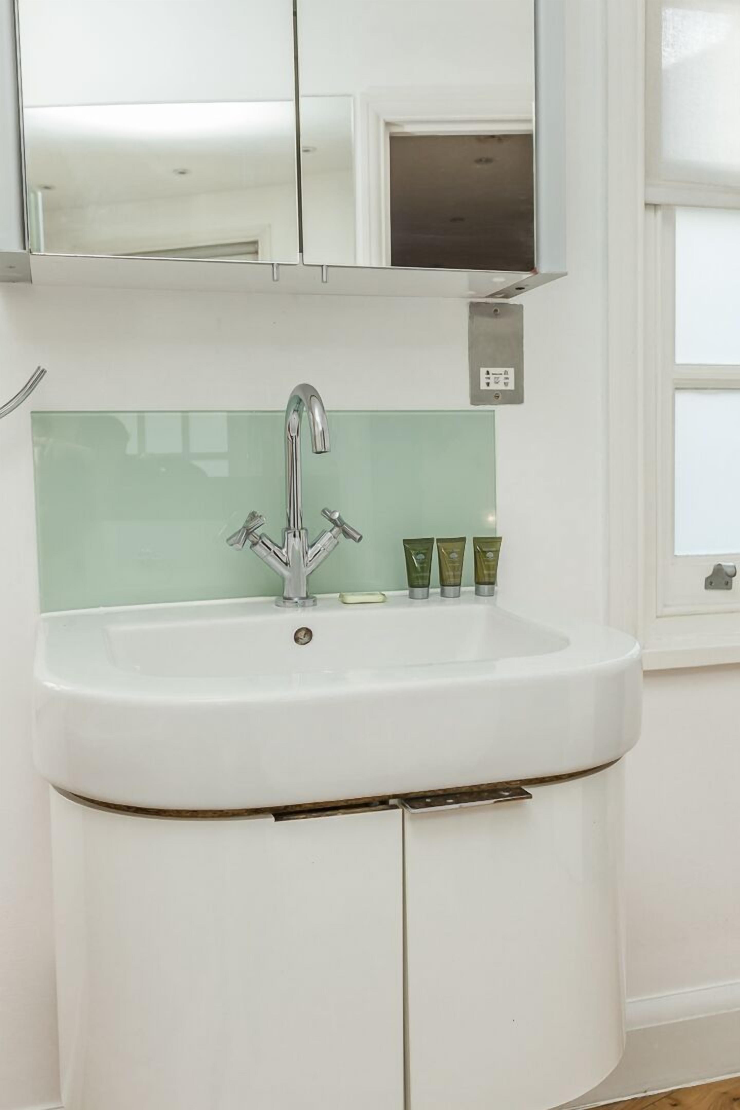 Un baño blanco con un lavabo, un salpicadero con azulejos verdes y un espejo sobre el lavabo.