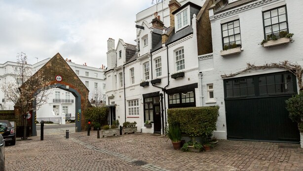 A cobblestone courtyard with a brick archway, white buildings, and potted plants. - Gorgeous house in the heart of Chelsea (London)