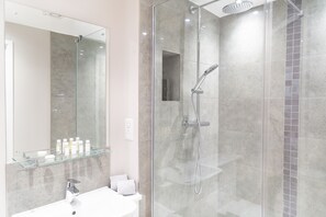 Une salle de bain moderne avec une douche à parois de verre, une étagère en verre où sont rangés les articles de toilette et un lavabo blanc.