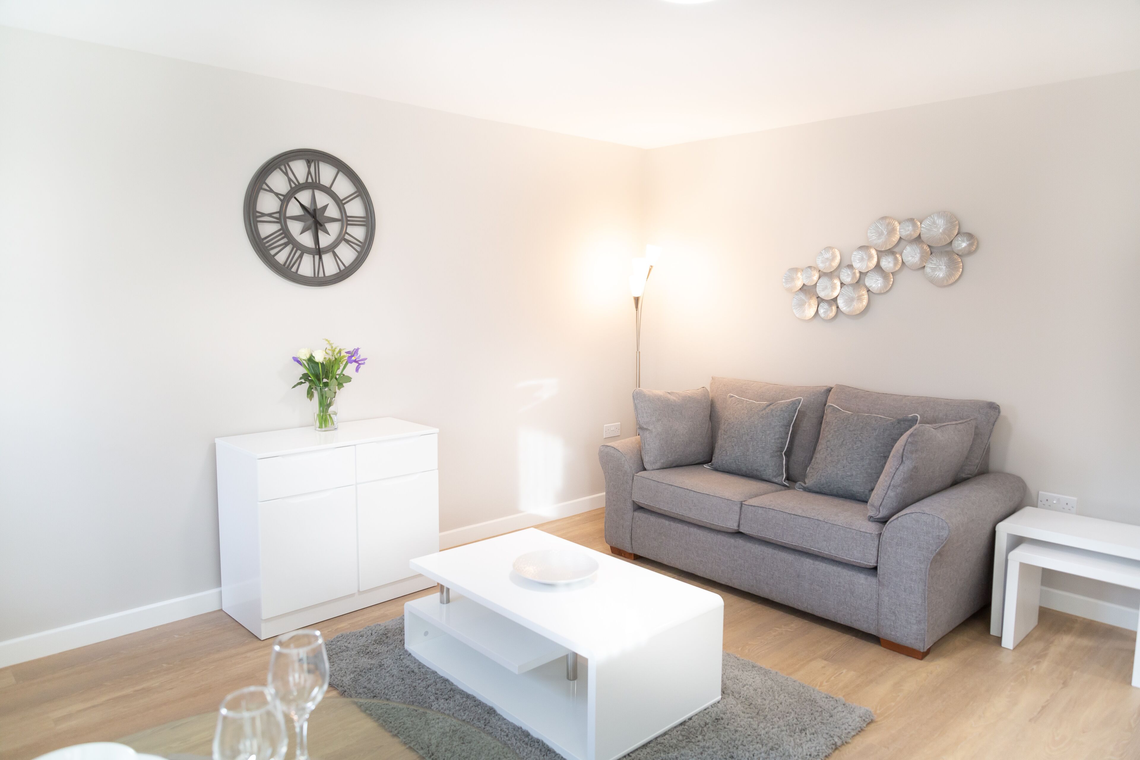 Ein modernes Wohnzimmer mit grauem Sofa, weißem Couchtisch und einer Wanduhr.