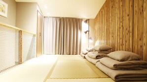 A room with a tatami mat floor, a bed with neatly folded blankets, a wooden wall, and a curtain partially drawn. - Ueno Lucky Homes (Tokyo)