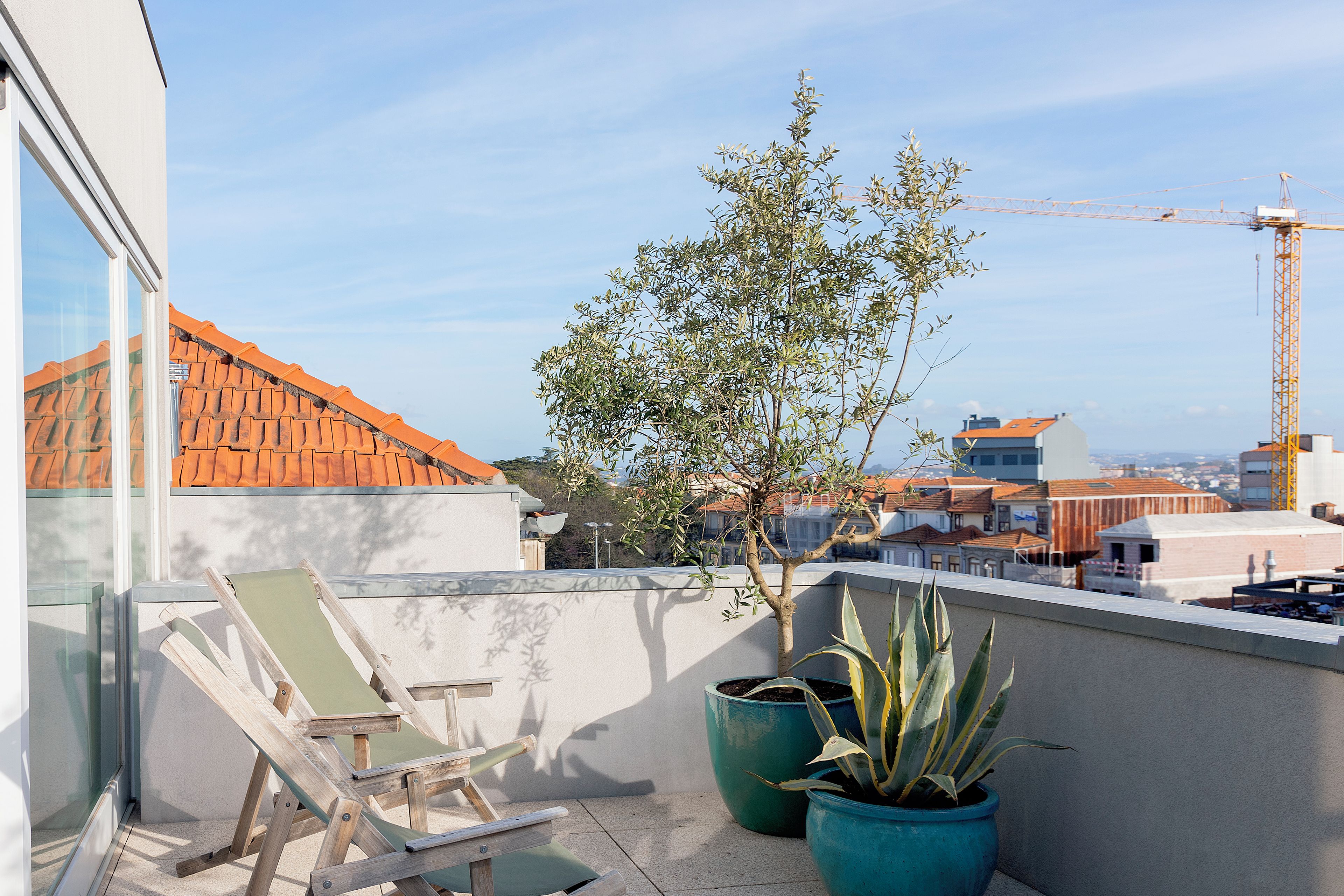 A balcony with a view of buildings, a tree, and a construction crane.