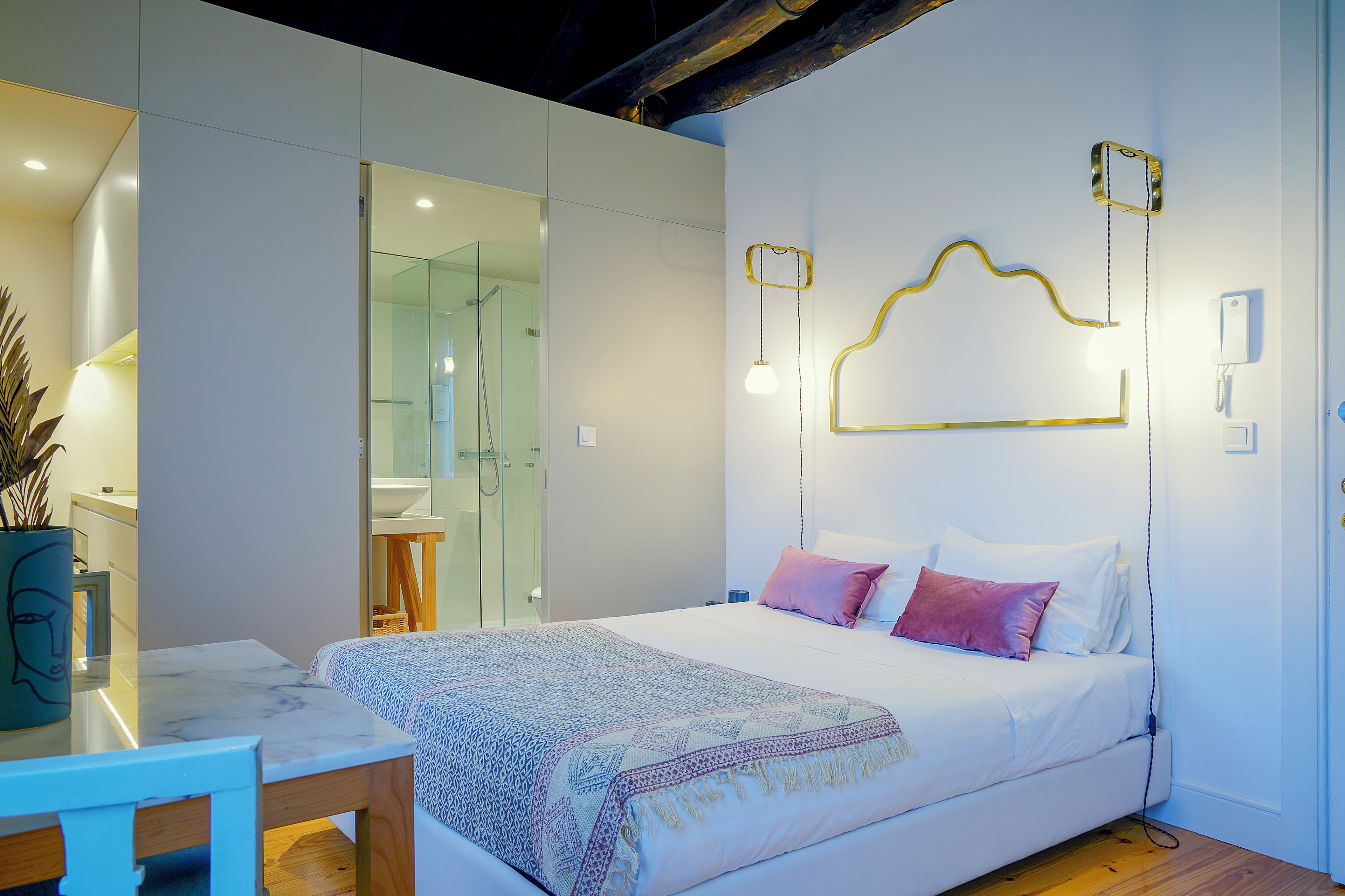 A modern bedroom with a glass shower enclosure, a bedside table, and a bed with patterned bedding.