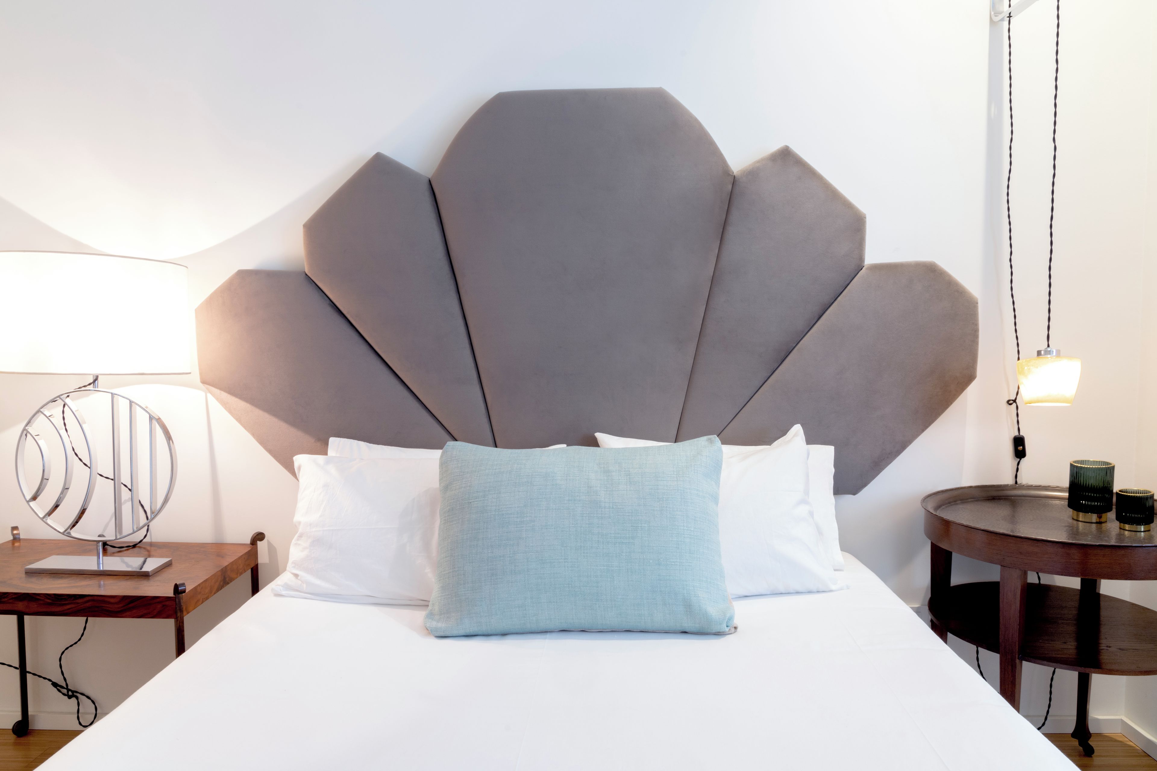 A bed with a large, geometric headboard, a bedside table with a lamp, and a small round table with two candles.