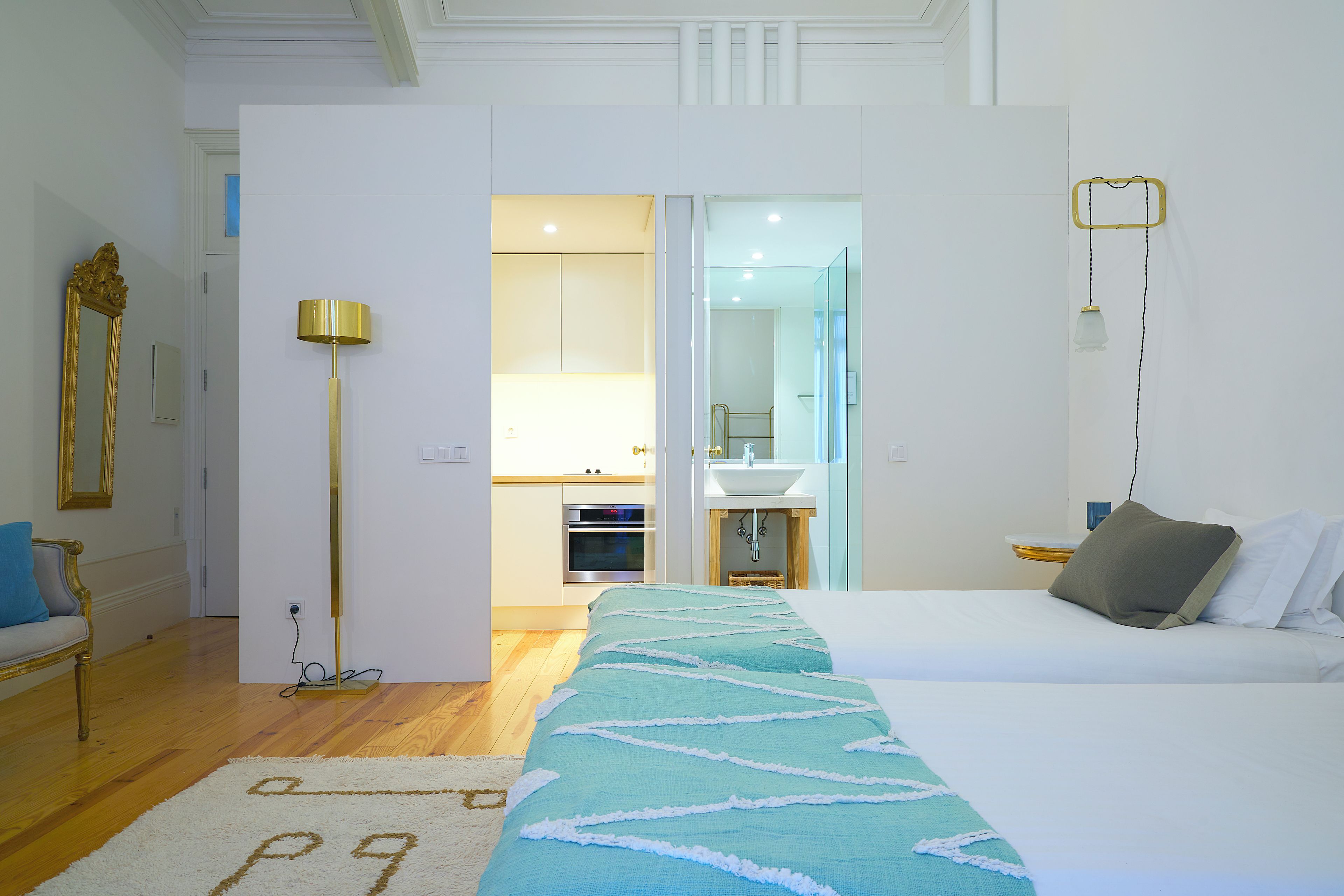 Habitación de hotel con cama, mesita de noche, lámpara, espejo y vista al baño.