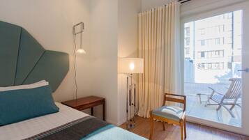 A hotel room with a bed, a chair, a lamp, and a view of the outside balcony.