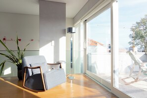 A modern room with a large sliding glass door, a wooden floor, a patterned armchair, a tall floor lamp, and a potted plant. - The Art Porto (Porto)