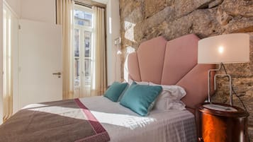 Een slaapkamer met een stenen muur, een bed met een roze hoofdeinde, teal kussens en een bedlampje.