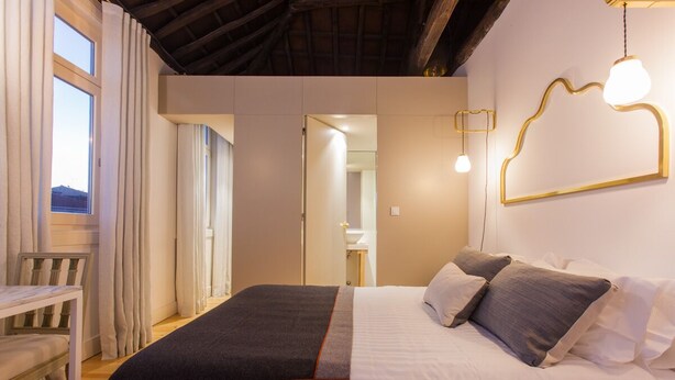 A bedroom with a bed, bedside tables, a wardrobe, and a view of a bathroom. - The Art Porto (Porto)
