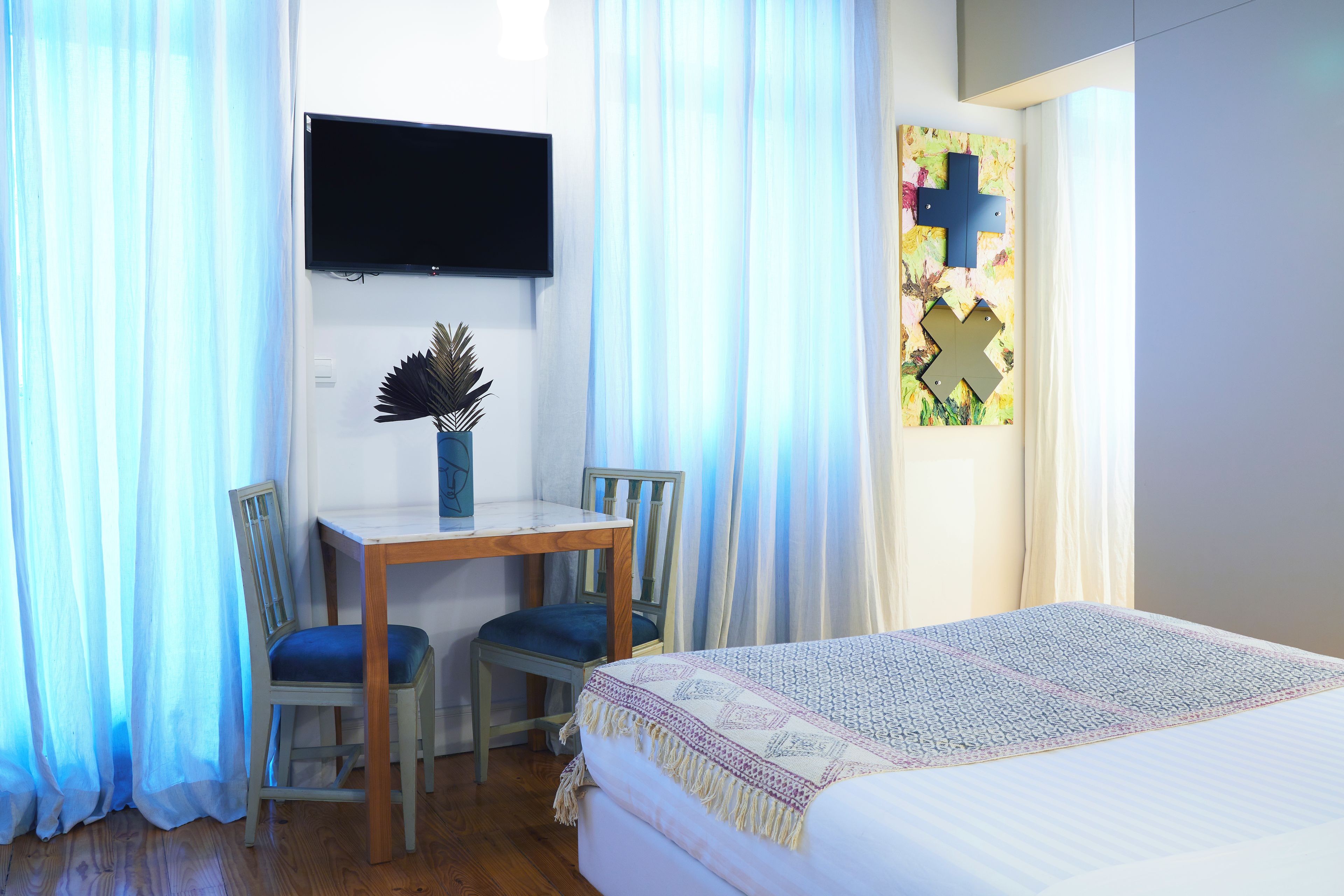 Une chambre comprenant un lit, un bureau avec deux chaises, un téléviseur fixé au mur et une fenêtre avec des rideaux.