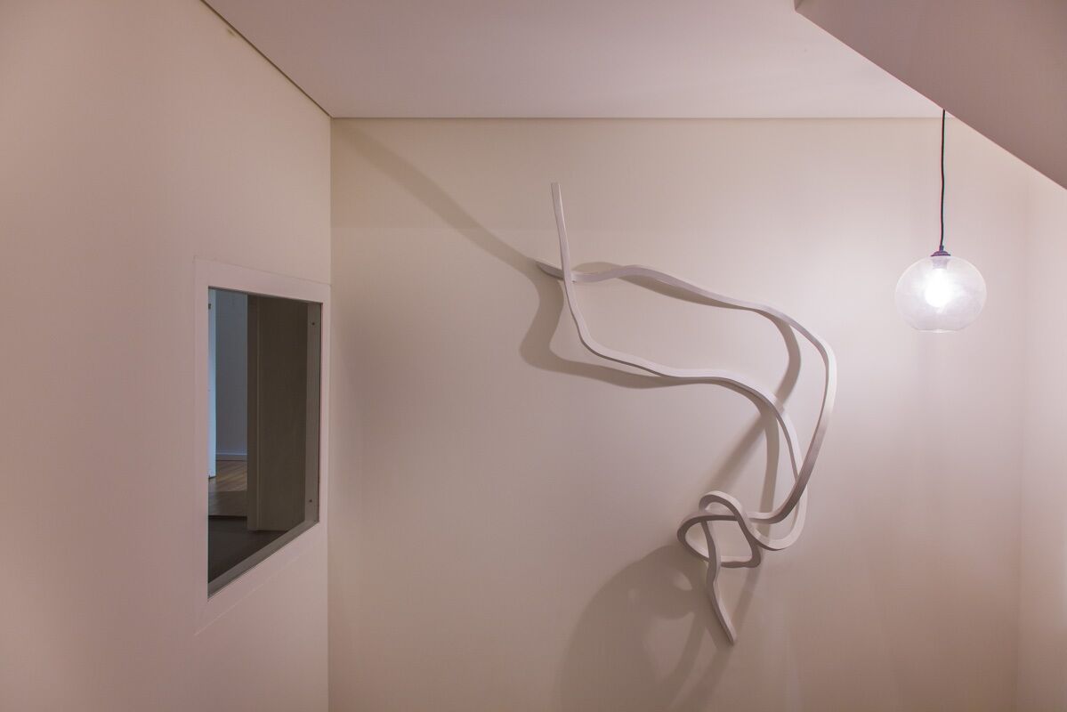 A minimalist interior with a white wall, a small window, and a single pendant light.