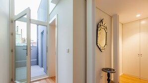A hallway with a glass door leading to a balcony, a decorative mirror, and a cabinet. - The Art Porto (Porto)