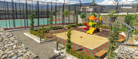 Un parque infantil con tobogán y estructuras para escalar, rodeado por una valla y con vistas a las montañas.