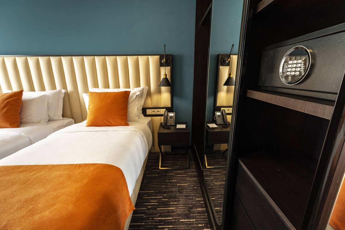 A hotel room with two beds, a minibar, a telephone, and a mirror.
