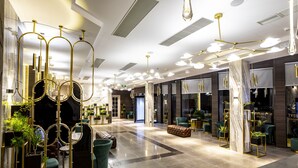 Eine moderne Hotellobby mit einer Marmorsäule, grünen Polstersesseln und goldenen Akzenten.