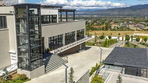 Ein modernes Gebäude mit Glasfassade, einem überdachten Außenbereich und Blick auf eine Stadt sowie Berge im Hintergrund.