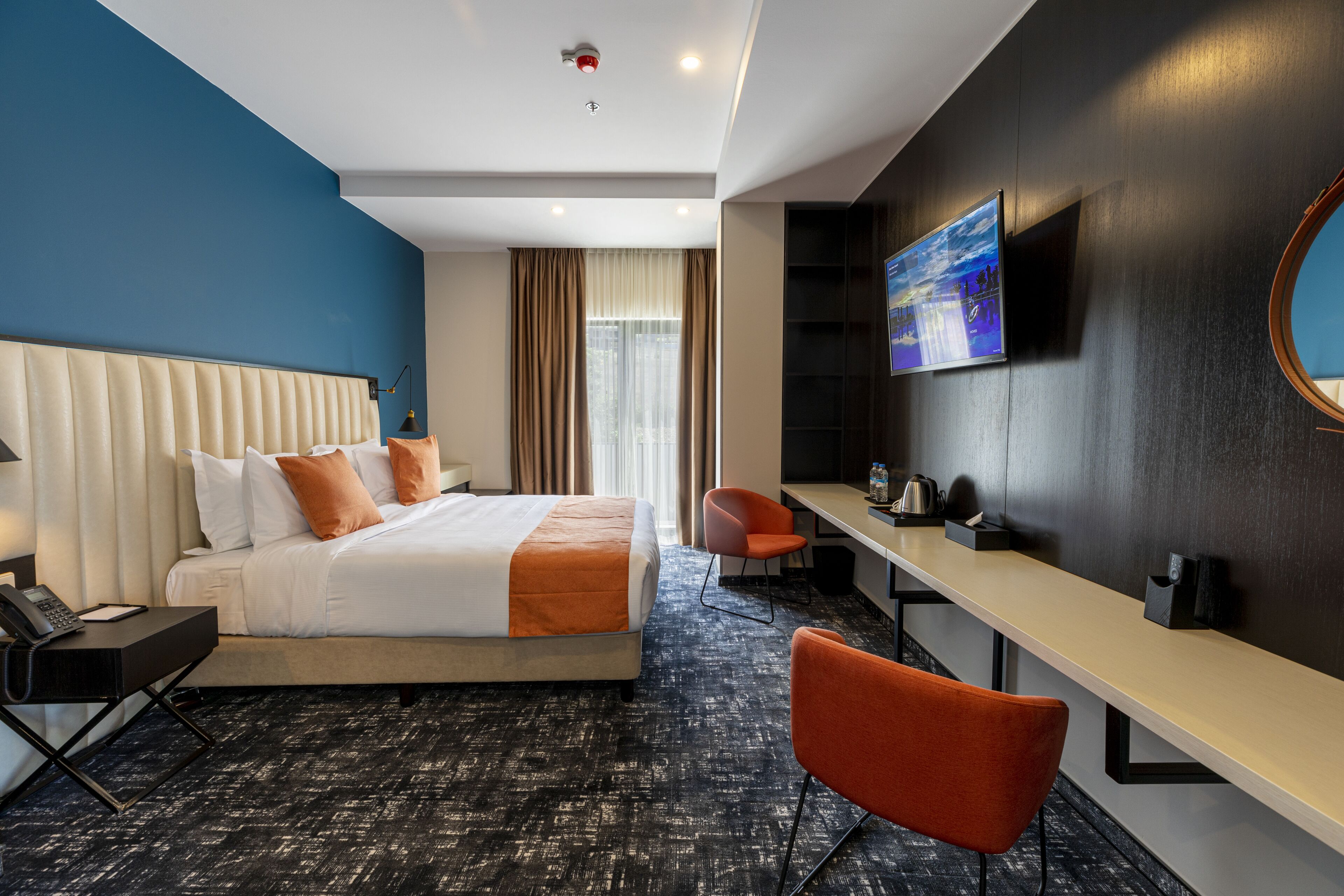 A hotel room with a bed, a desk, a chair, a TV, and a window with curtains.