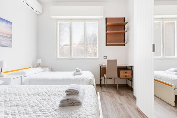 A hotel room with two beds, a desk, a chair, a wardrobe, and a window.