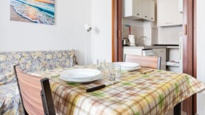A dining area with a table set for two, a sofa, and a kitchen in the background. - GuestHost - Lovely studio apartment complete with all major amenities (Milano)
