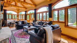 A spacious living room with a high ceiling and large windows, furnished with leather sofas and a coffee table. - Alpine Majesty (Breckenridge)