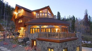 A large, multi-story wooden house with a stone foundation, large windows, and a balcony. - Alpine Majesty (Breckenridge)