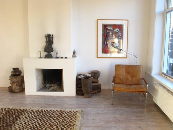 Una sala de estar con chimenea, una silla, un tapete y un cuadro en la pared.