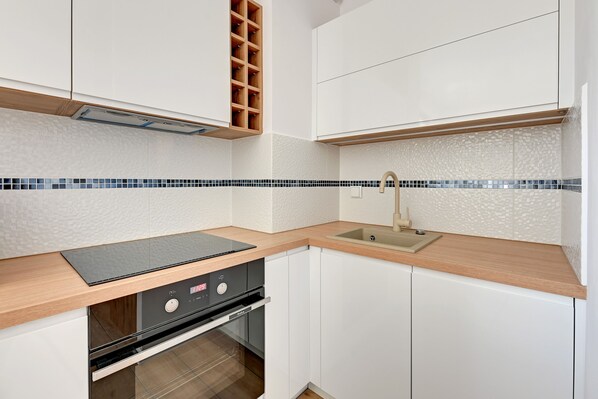 Eine moderne Küche mit weißen Schränken, einer Holzausziehtafel, einem eingebauten Ofen und einem Spülbecken mit Armatur.