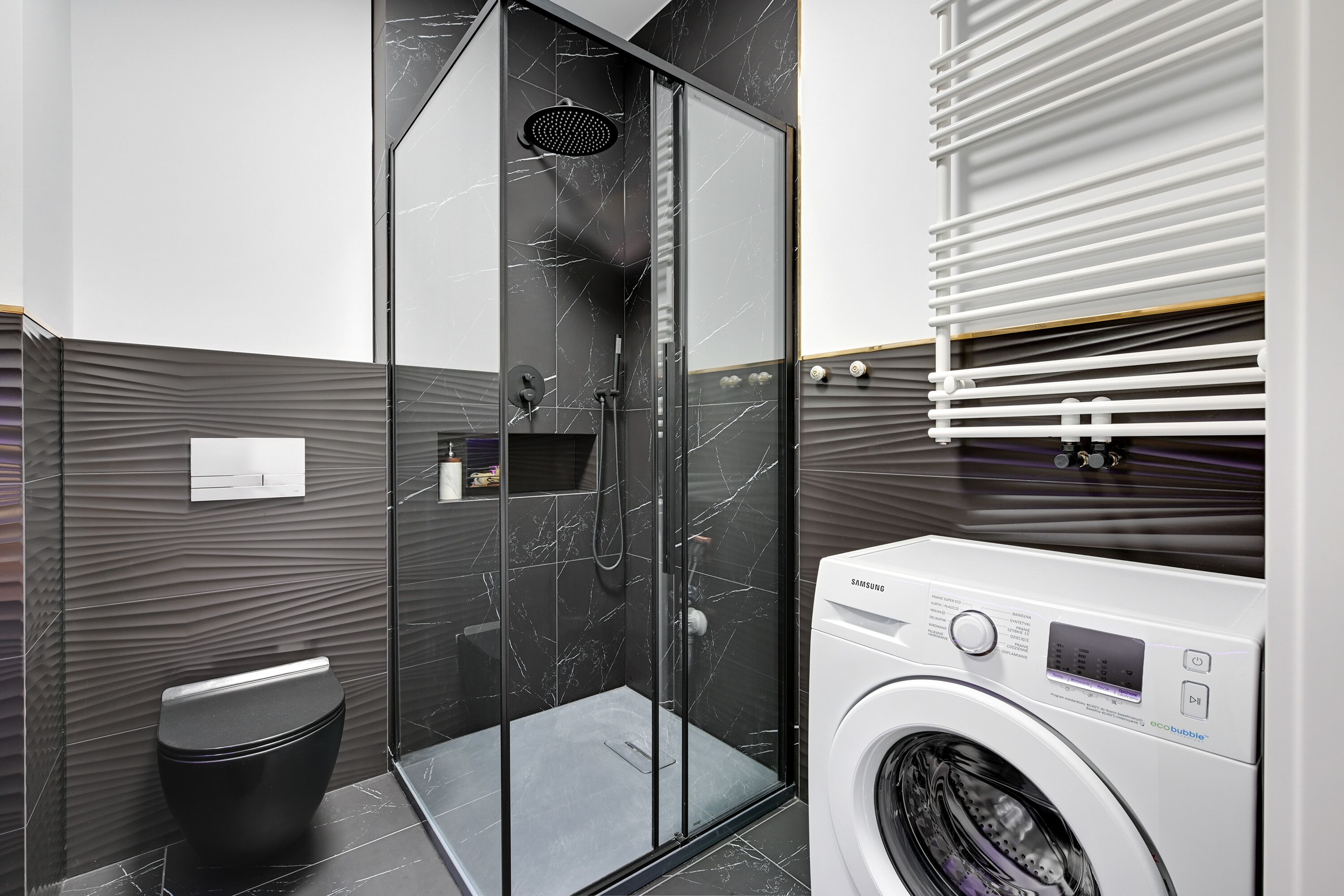 Ein modernes Badezimmer mit einer Duschkabine, einer schwarzen Toilette und einer Samsung Waschmaschine.