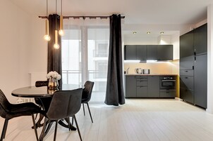Una cocina moderna con armarios oscuros, un comedor con mesa y sillas redondas, y un amplio ventanal con cortinas traslúcidas.