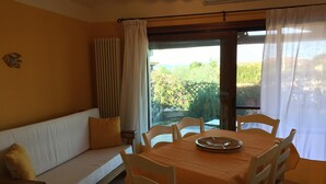 A dining area with a table set for four, a sofa with cushions, and a view of greenery outside. - Casa Vacanze Aria (Budoni)