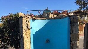 A blue outdoor shower enclosed by stone walls, with a metal grate at the bottom. - Casa Vacanze Aria (Budoni)