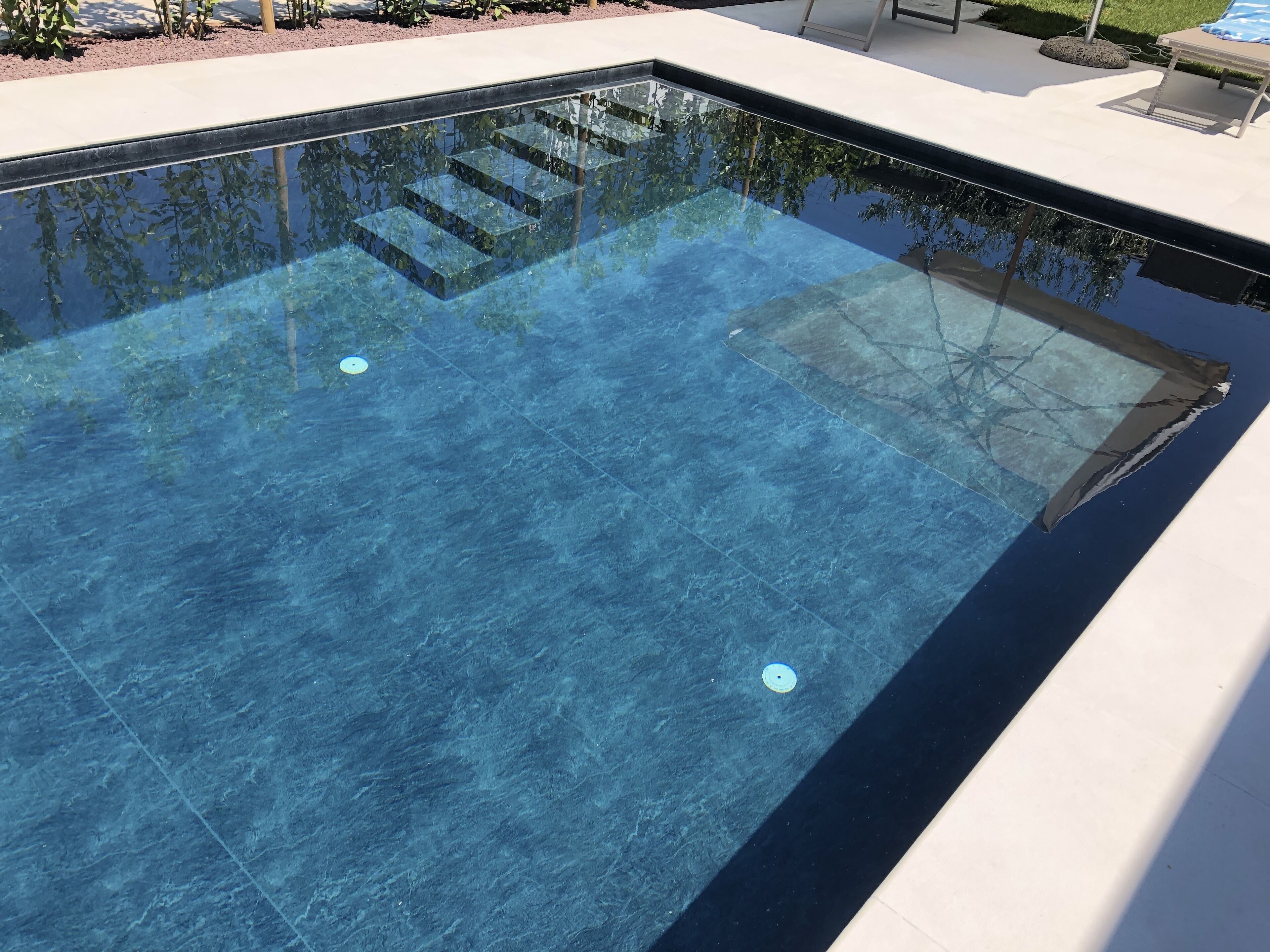Une piscine aux eaux cristallines, accessible par des marches, et entourée d’une terrasse blanche.