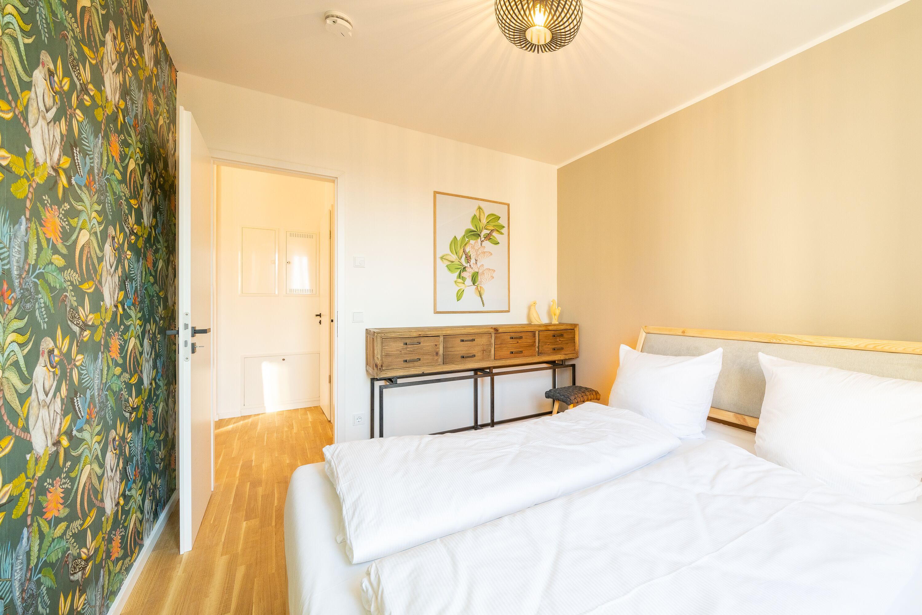 Een slaapkamer met een bed, een houten dressoir, een deur en een muur met een bloemenmotief.