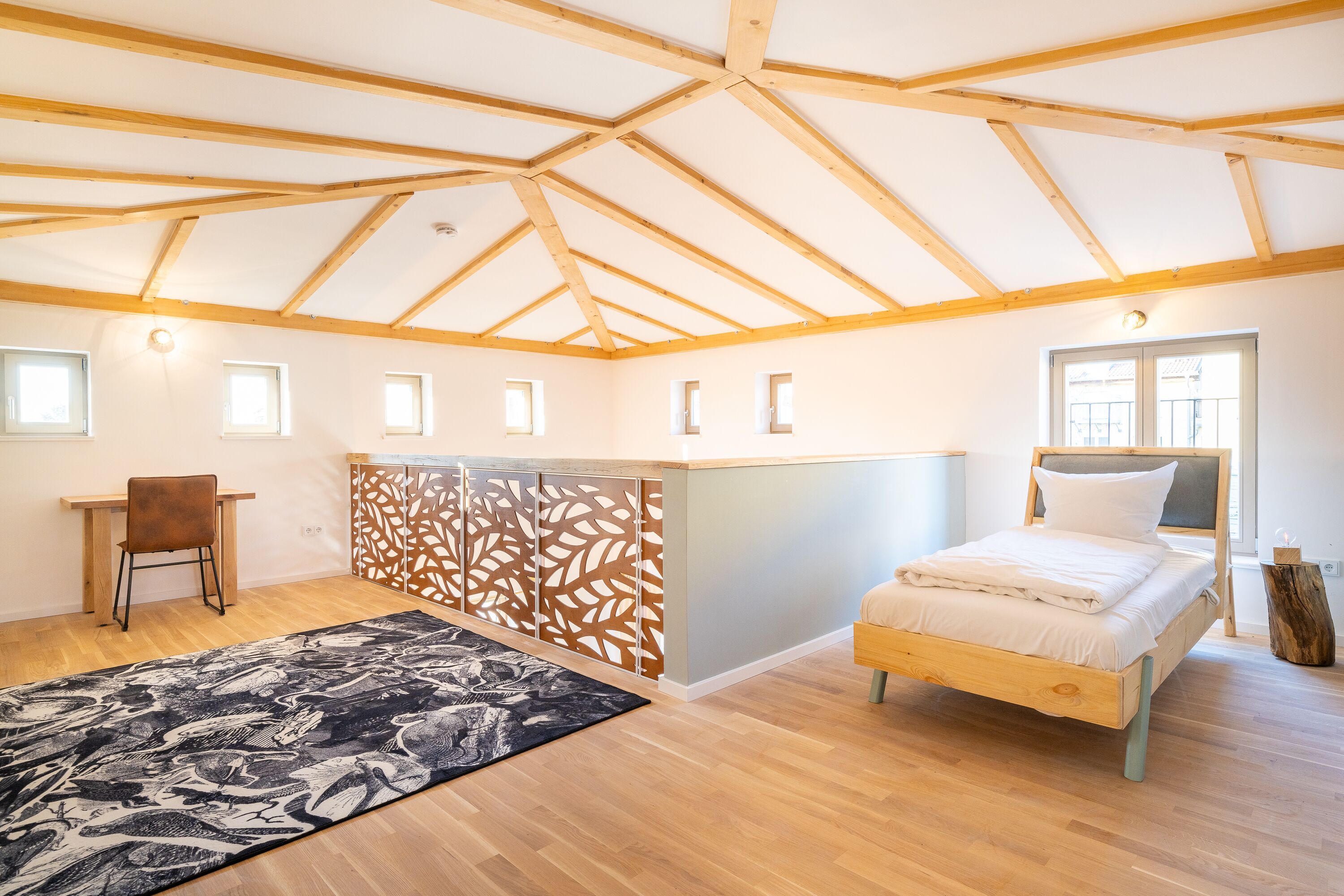 Un dormitorio con techo de madera, cama, escritorio y silla.