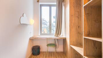 Une pièce d’angle avec un plancher en bois, une fenêtre avec des rideaux, un fauteuil vert et une étagère.