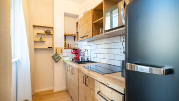 A compact kitchen with wooden cabinets, a black refrigerator, and a tiled backsplash.