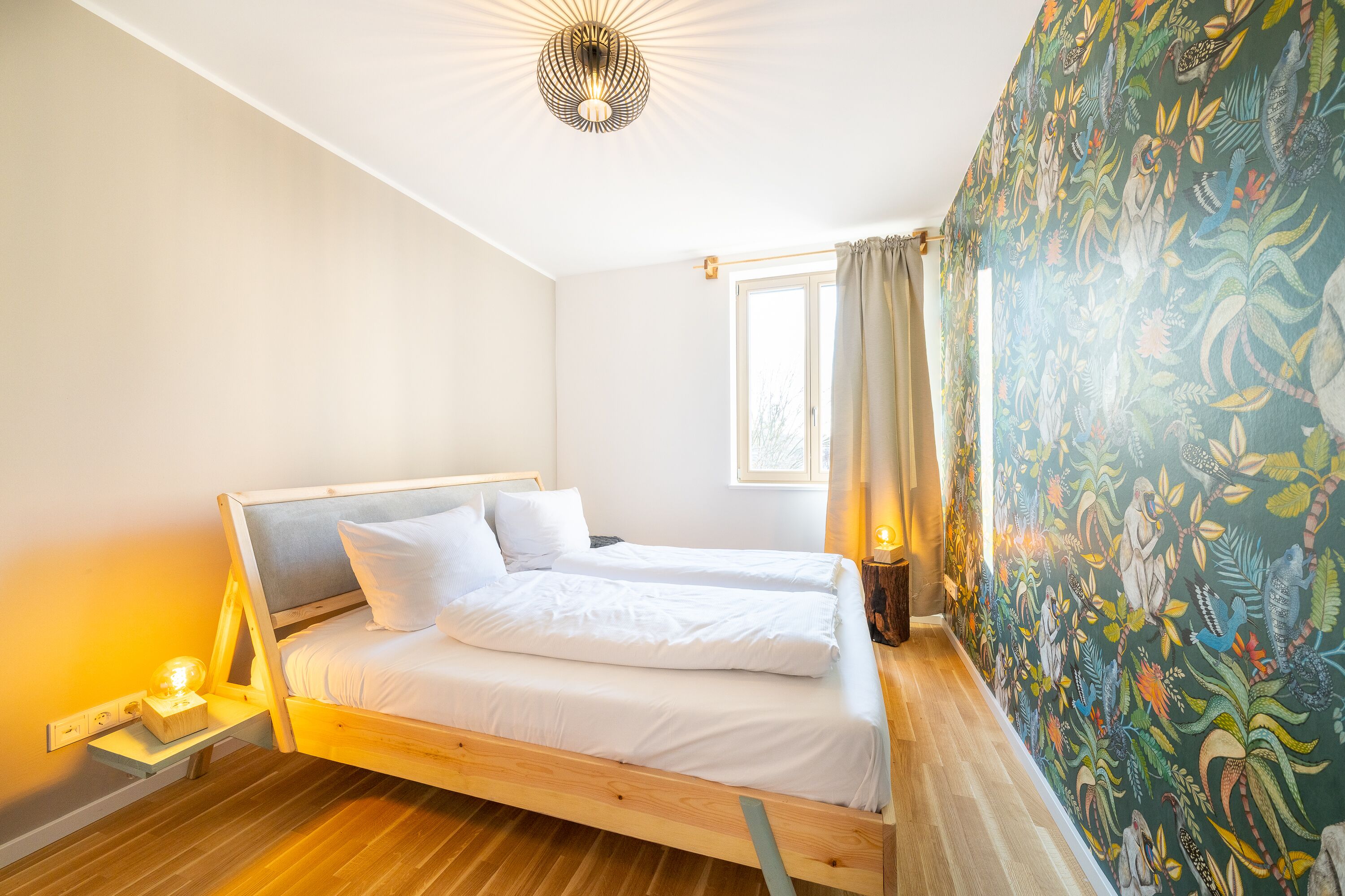 A room with a bed, a window with curtains, and a wall with a mural.