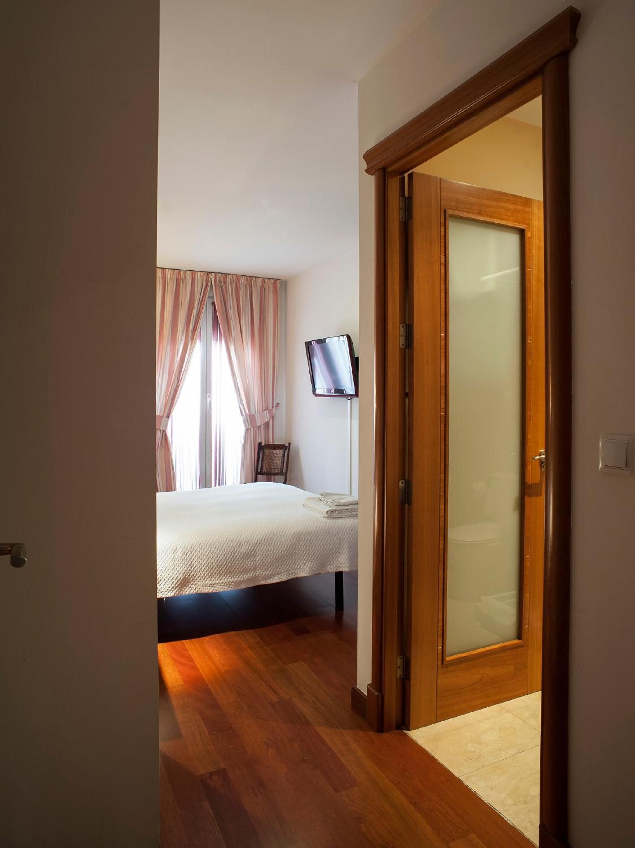 A bedroom with a bed, a TV, a wooden door, and a window with curtains.