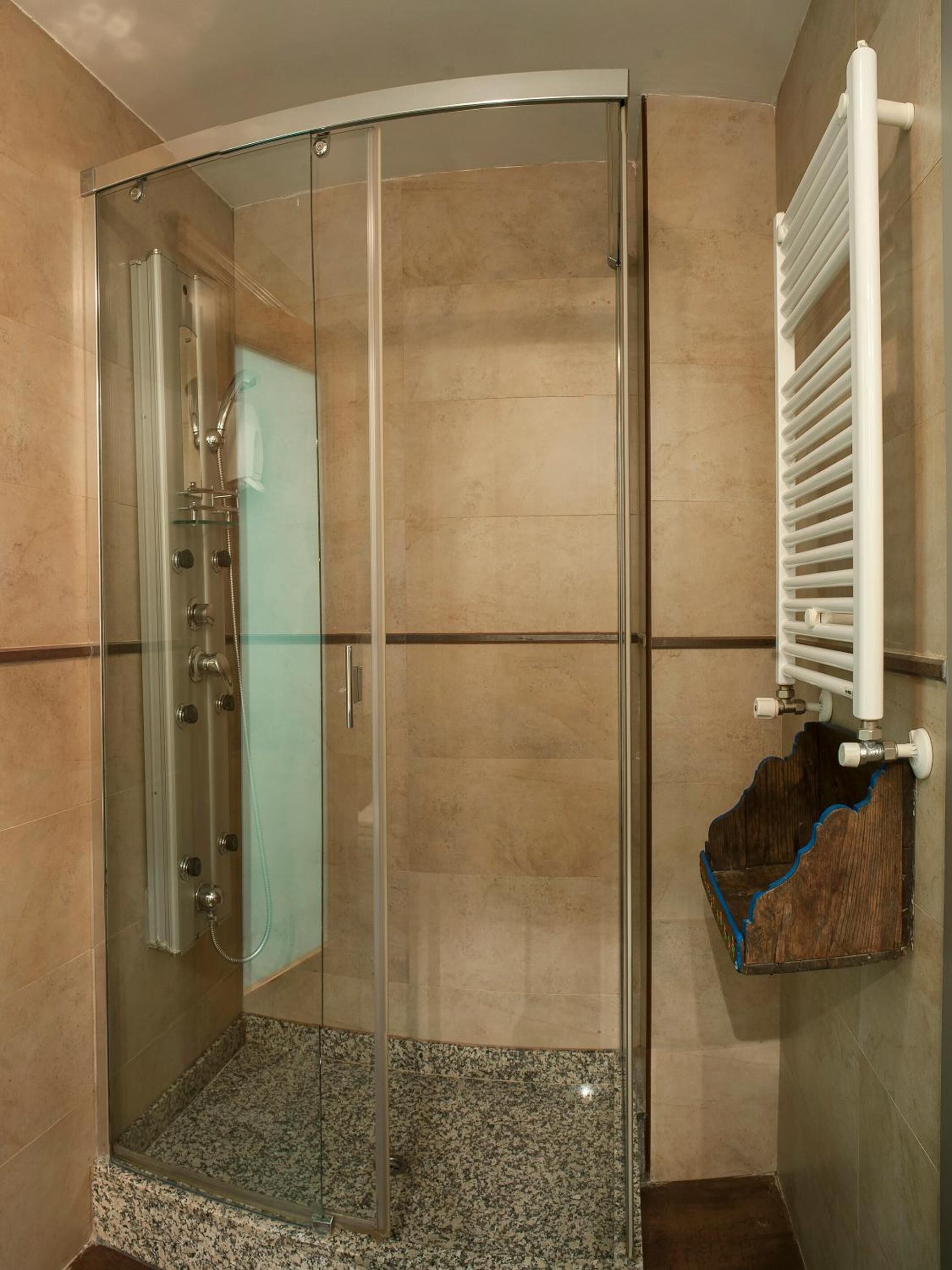 A glass-enclosed shower with a built-in towel rack and a corner radiator.