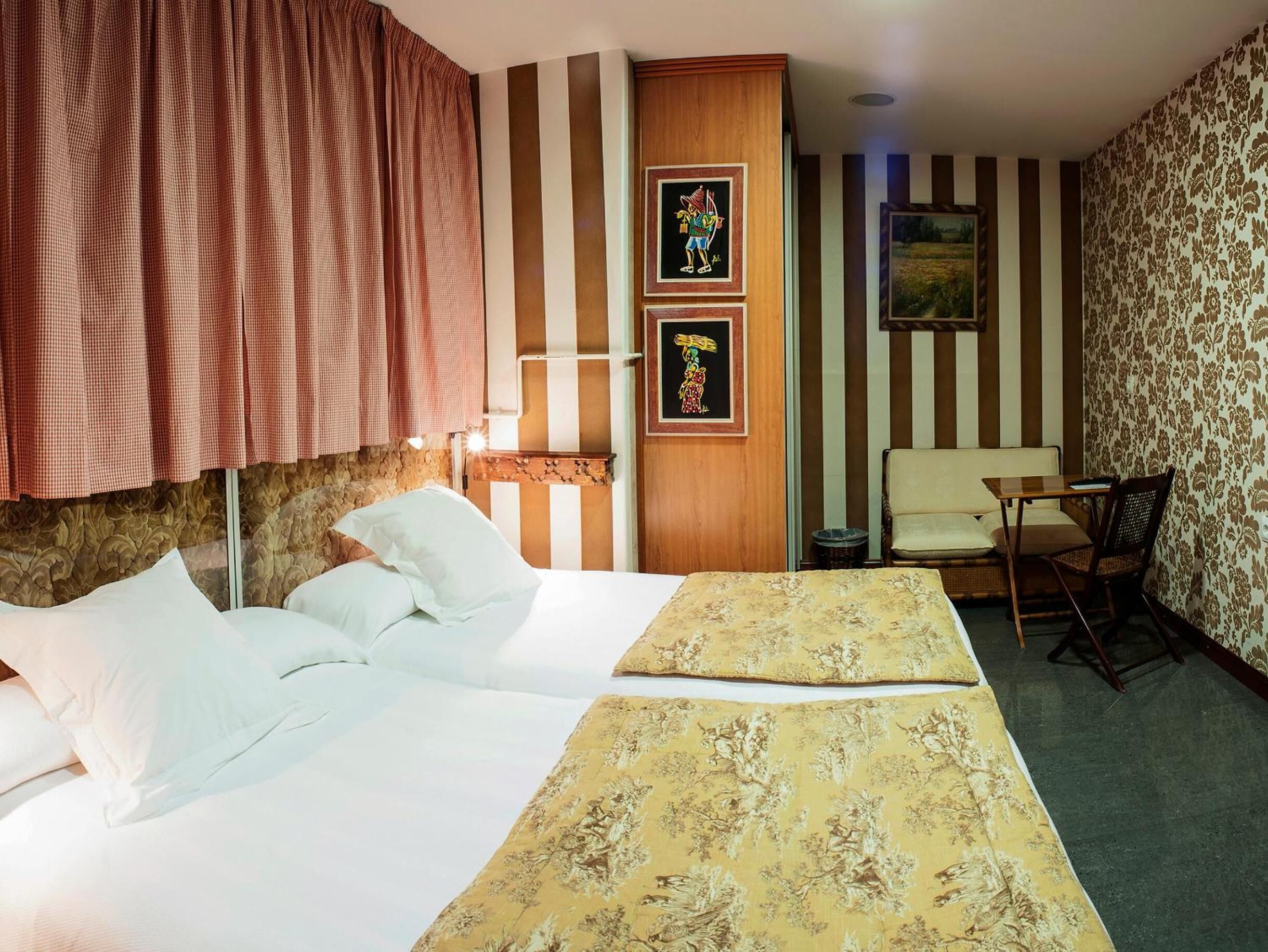 Habitación de hotel con una cama grande, una mesita pequeña, una silla y paredes a rayas.