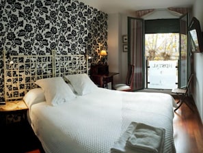 Ein Hotelzimmer mit einem großen Bett, einem Nachttisch, einem Sessel und Blick ins Freie.