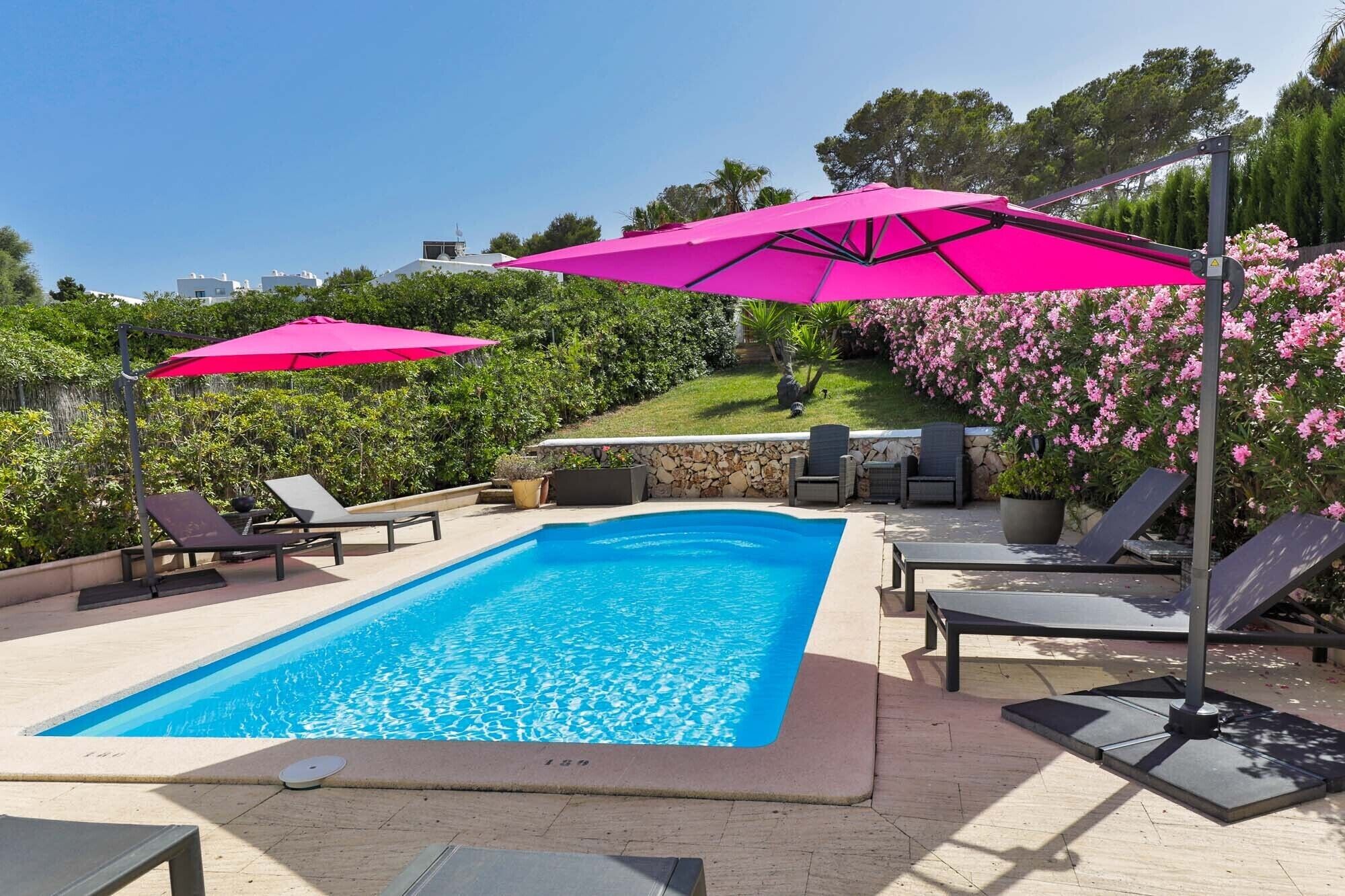 A rectangular swimming pool with a clear blue water surface, surrounded by lounge chairs and pink umbrellas.