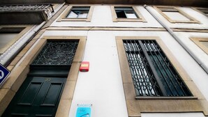 A building facade with a green door, a window with metal bars, and a blue sign with "OPORTO" and "SNU" on it. - Oporto Sky Hostel (Porto)