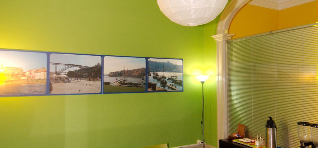 Una habitación con una pared verde, tres fotografías enmarcadas, una lámpara de pie y una ventana con persianas.