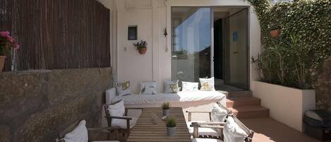 A sunlit outdoor seating area with a wooden table and chairs, a sofa, and potted plants.