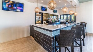 A bar area with a counter, bar stools, hanging light fixtures, and a television screen.