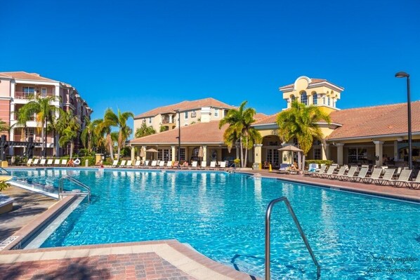 A swimming pool with lounge chairs and palm trees, surrounded by multi-story buildings with balconies. - Vista Cay Jewel (Orlando)